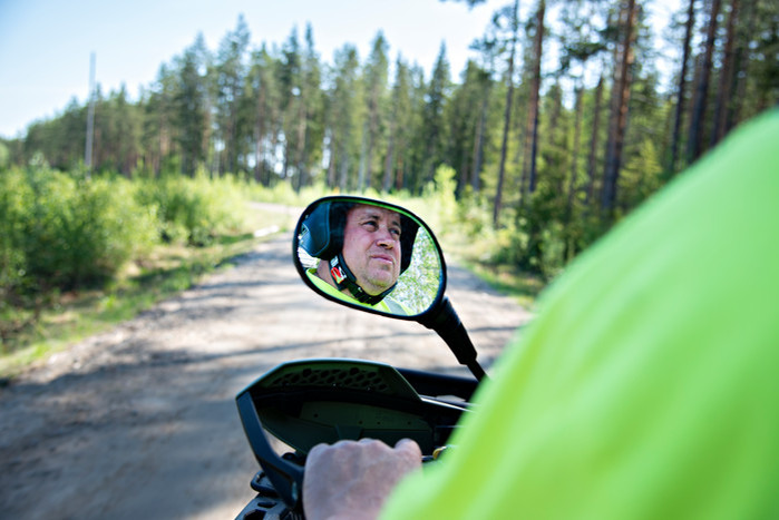 Man syns i backspegel på sexhjuling medan han kör längs en grusväg i skogen.