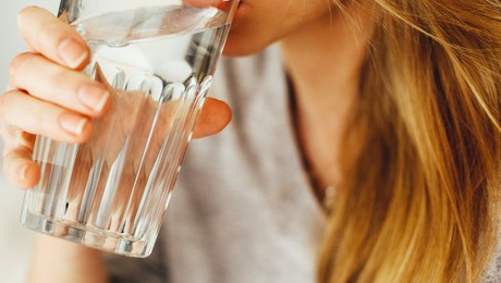 En kvinna med långt hår dricker vatten ur ett glas.