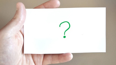 En person håller i ett vitt kort med ett grönt frågetecken på.